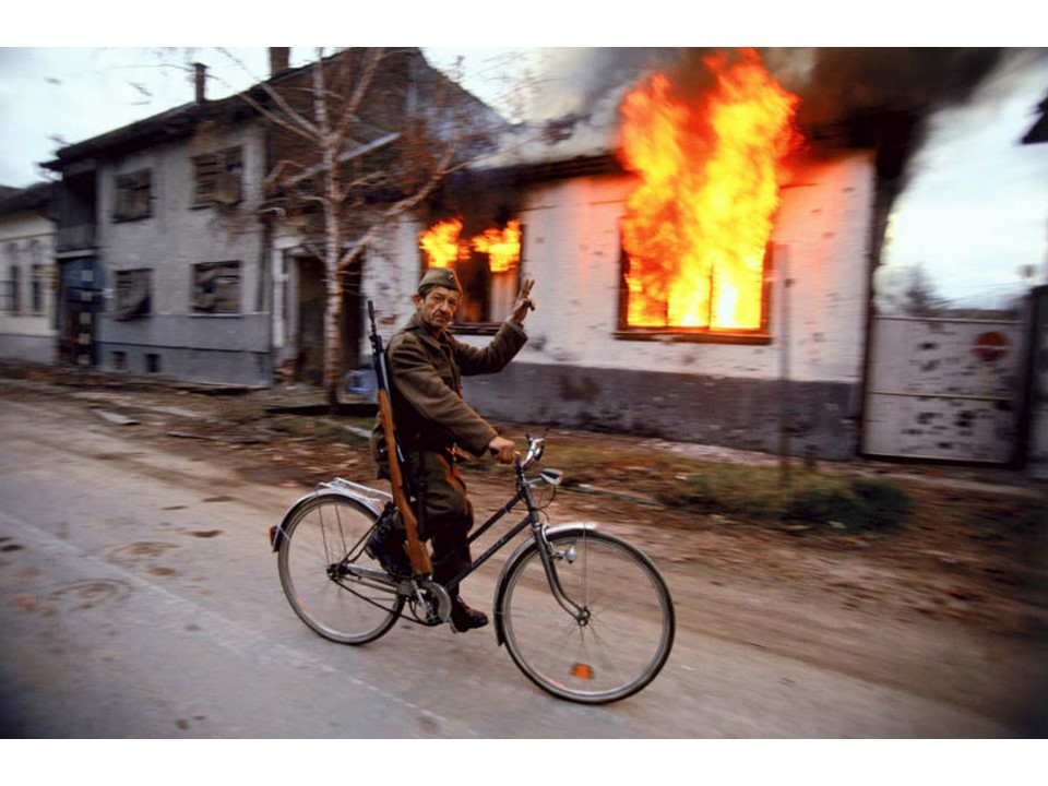 Blood and Honey: A Balkan War Journal
Soldiers and Paramilitaries - A Serbian soldier cycles by a burning house on the destroyed streets of Croatian city of Vukovar, Nov. 24, 1991.
ronhaviv.com
